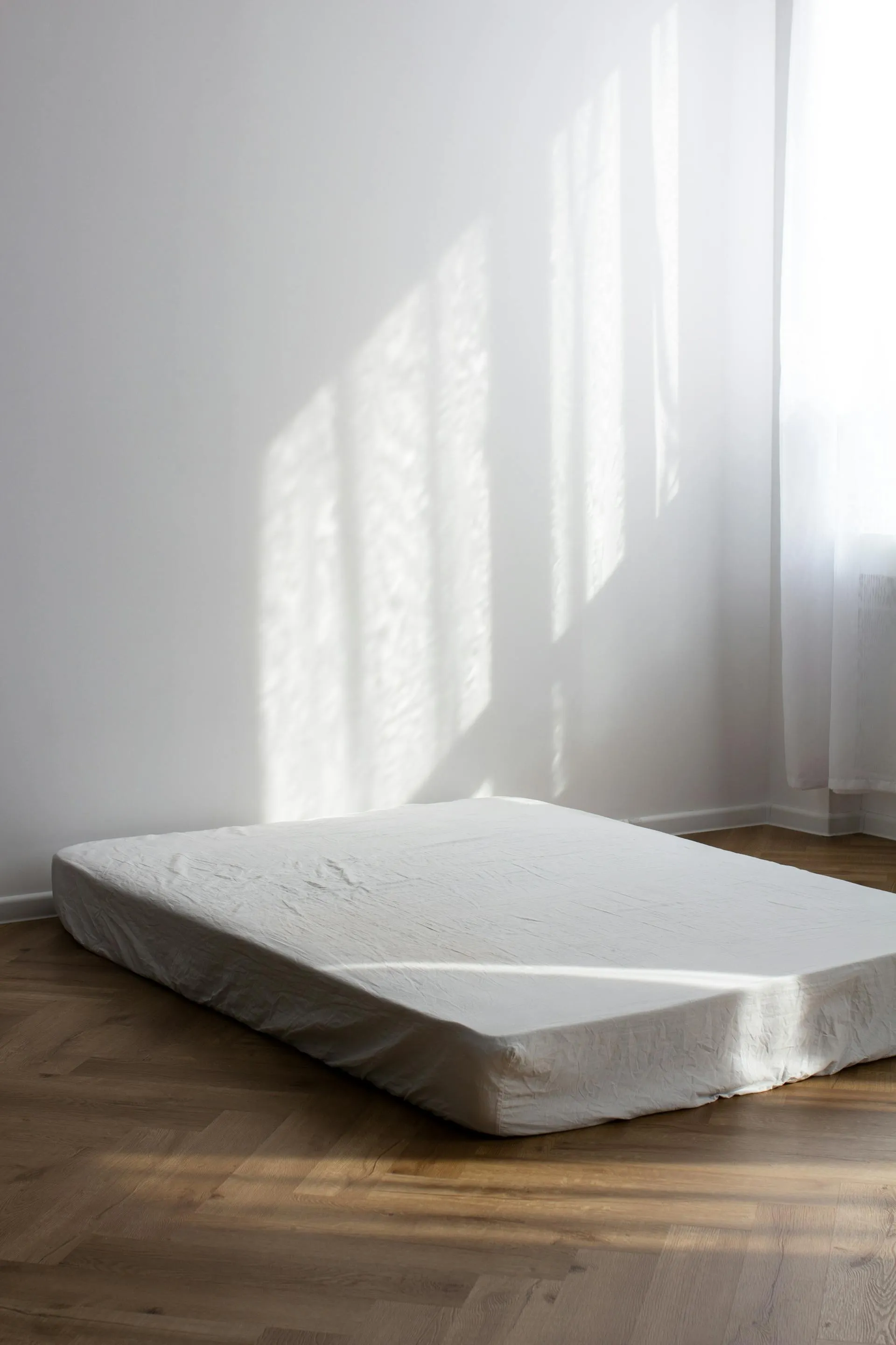 Minimalist bedroom interior showing a single mattress receiving soft natural light through a window