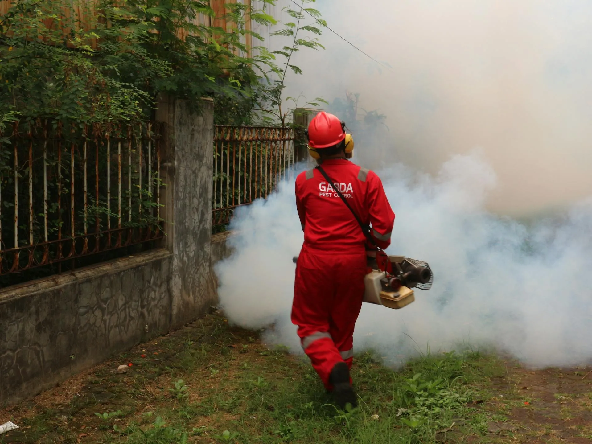 Pest control technician fogging an outdoor residential yard with smoke during an active treatment