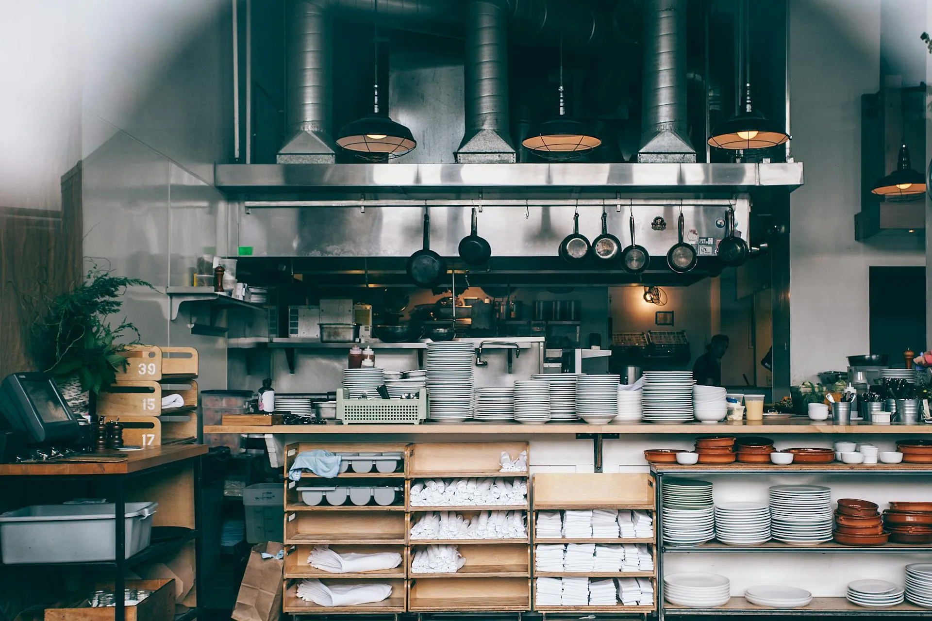 Stainless steel commercial restaurant kitchen interior showing food preparation surfaces and dry-store shelving