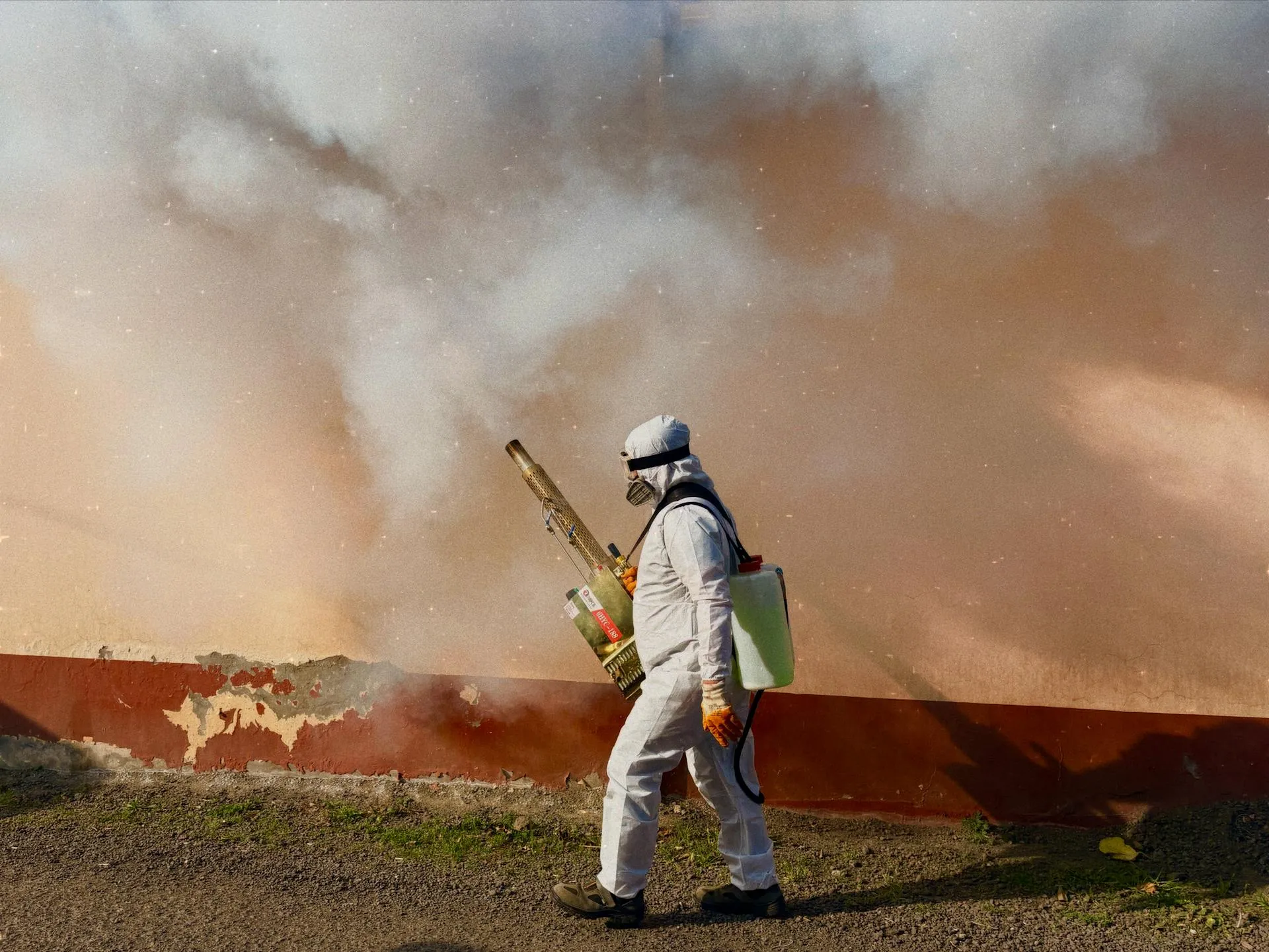 Pest control worker in full protective suit and respirator performing residential fumigation treatment outdoors