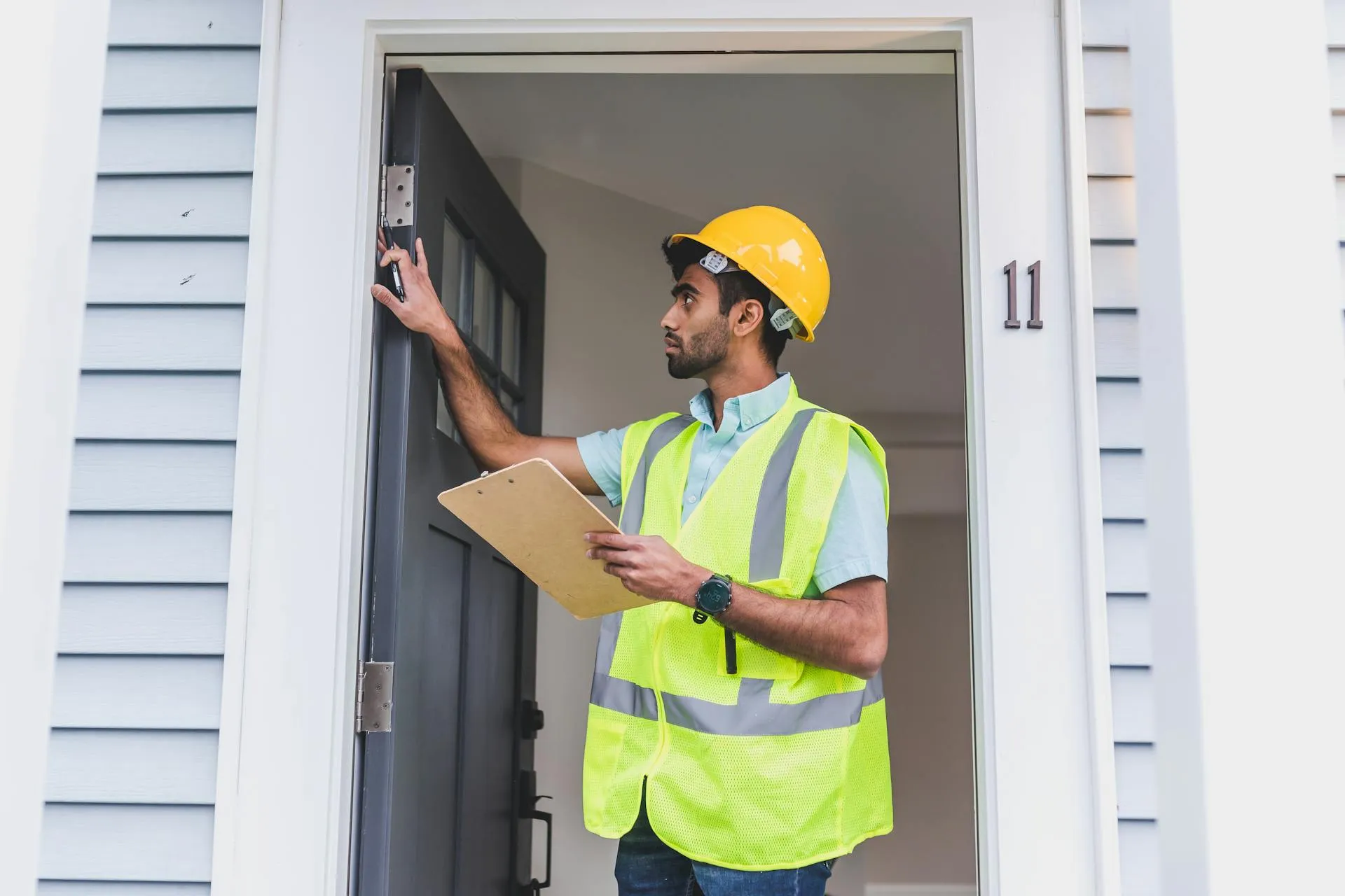 Home inspector in safety vest and hard hat checking a doorframe with clipboard during a property inspection